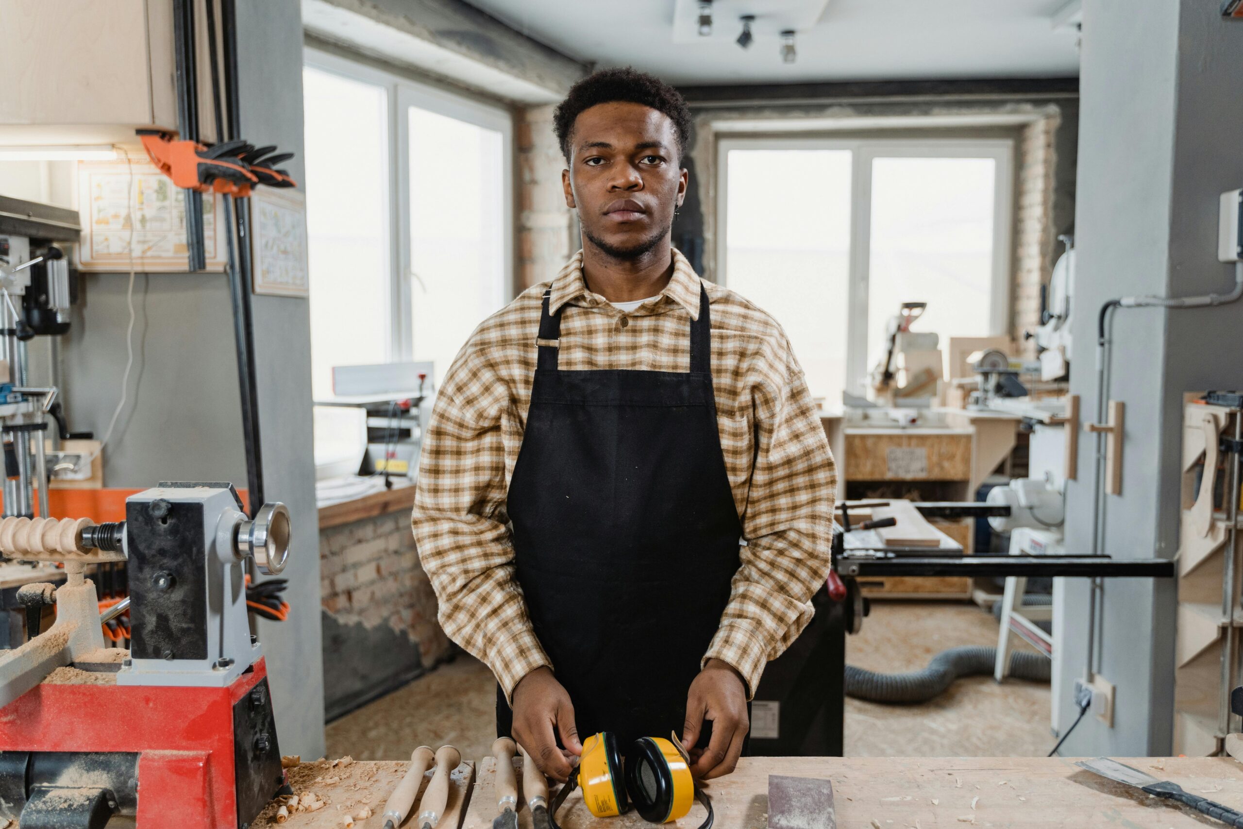 Portrait of a focused African American woodworker in an apron standing in a workshop.